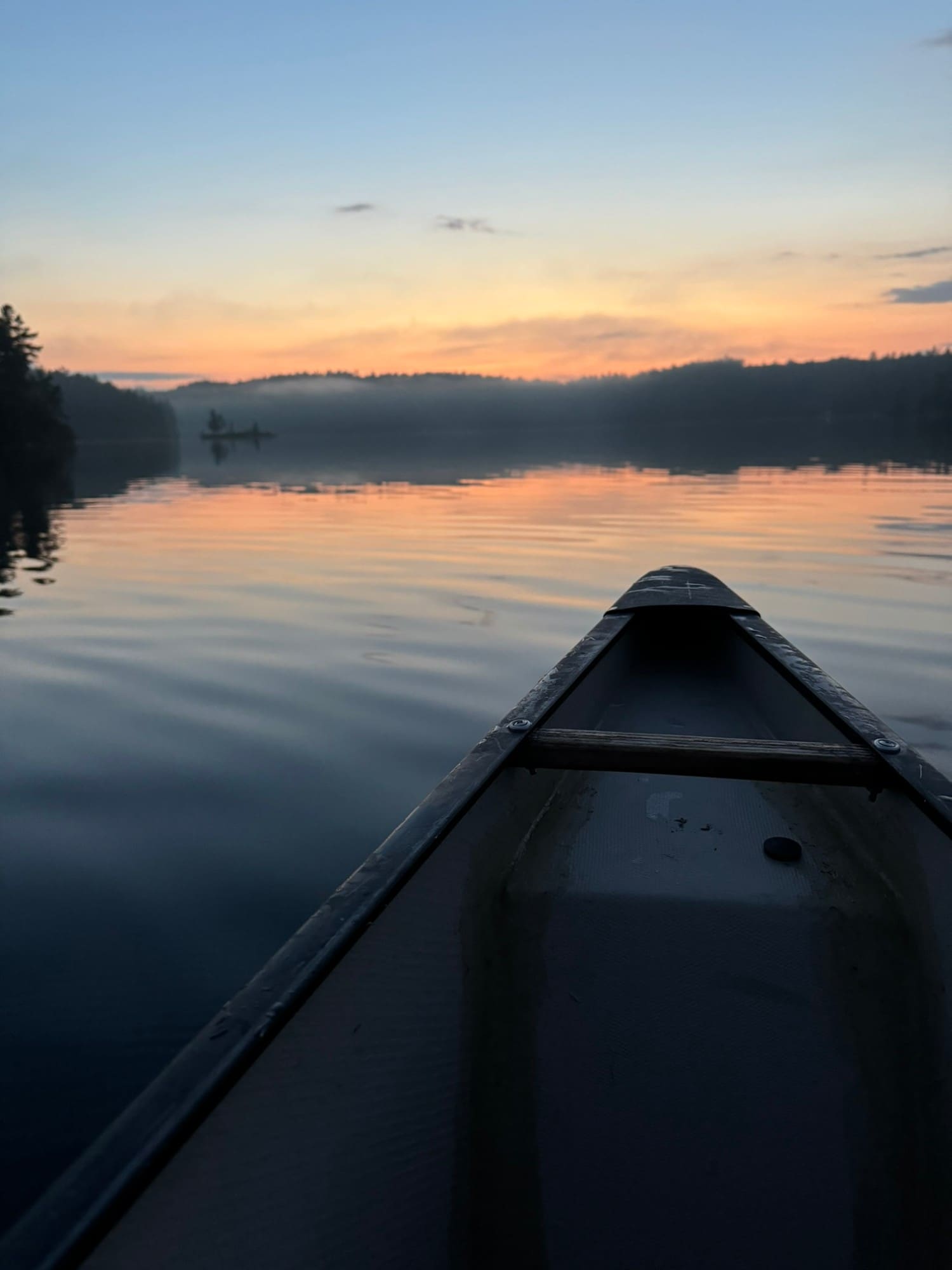 View from the bow of a canoe on a calm lake at sunset